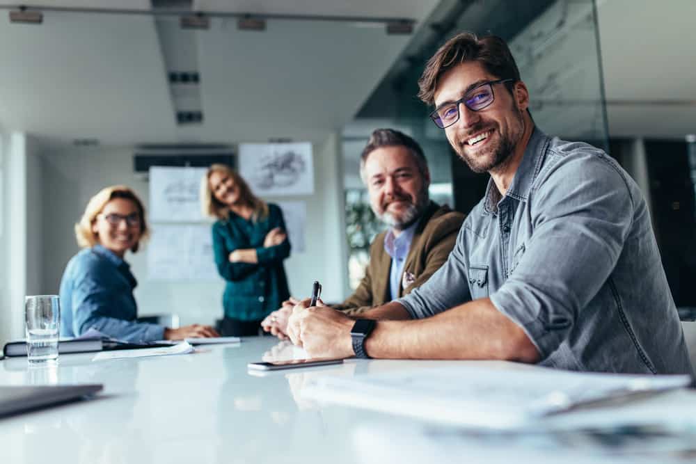 Office staff sitting around table smiling at camer